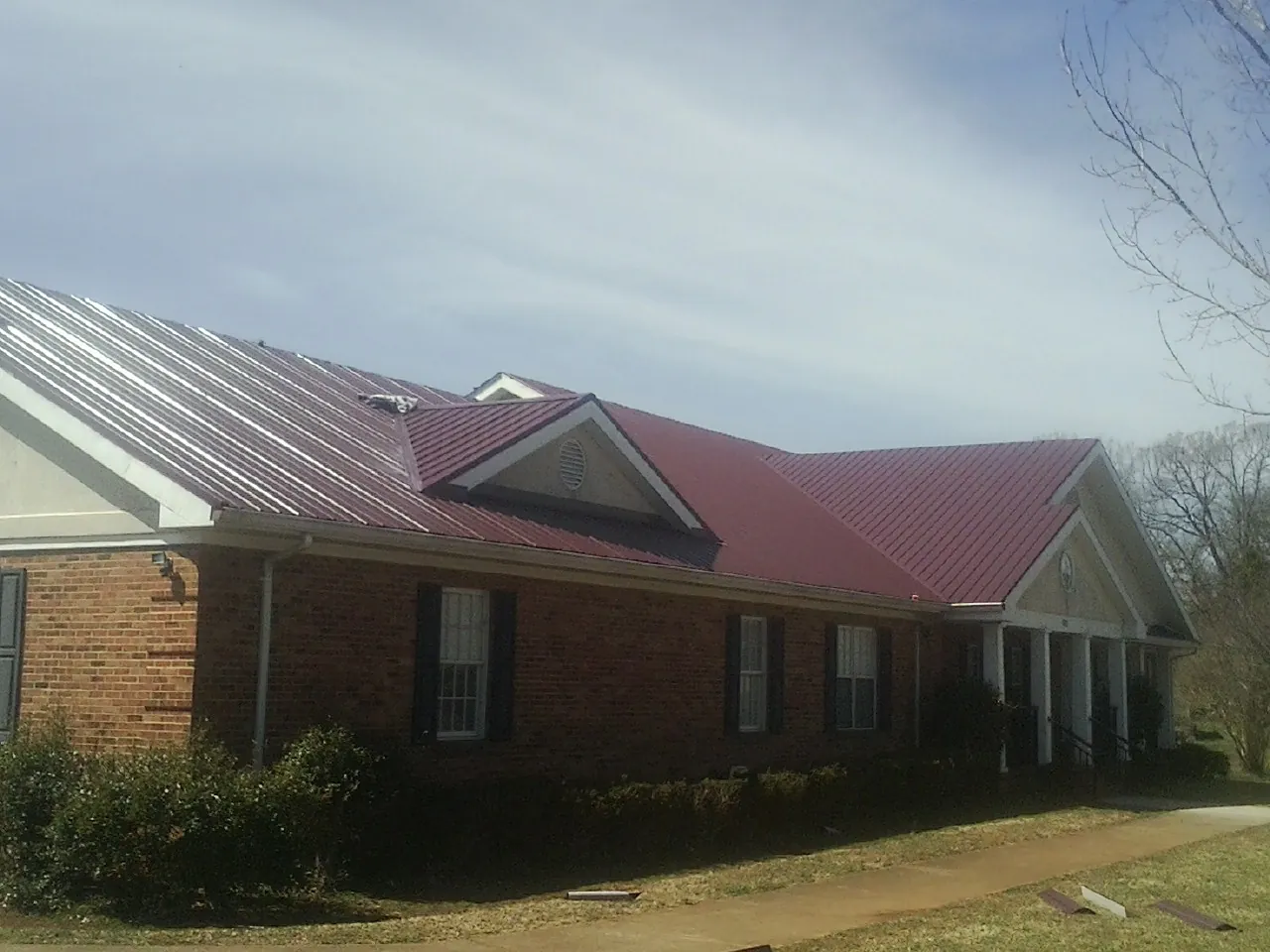 Red metal roof with gabled entries on a long brick building, from a Hail Damage Roof Repair job in Tidioute