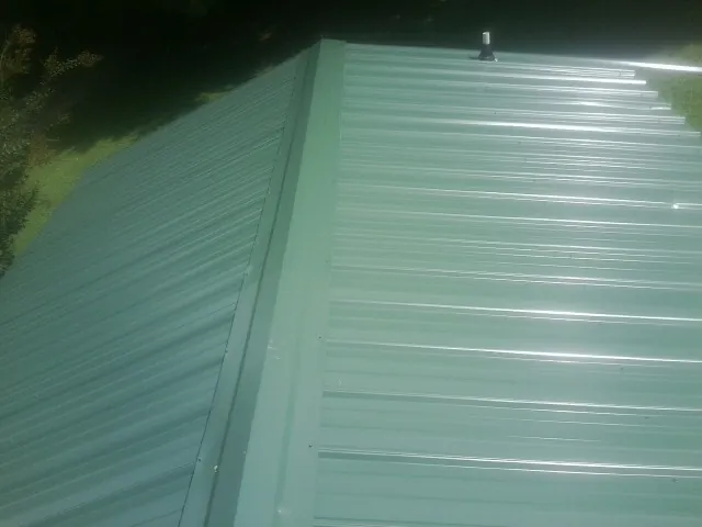 New green metal panels meeting at the ridge of a roof — Flat Roof Repair work by our crew in Tidioute