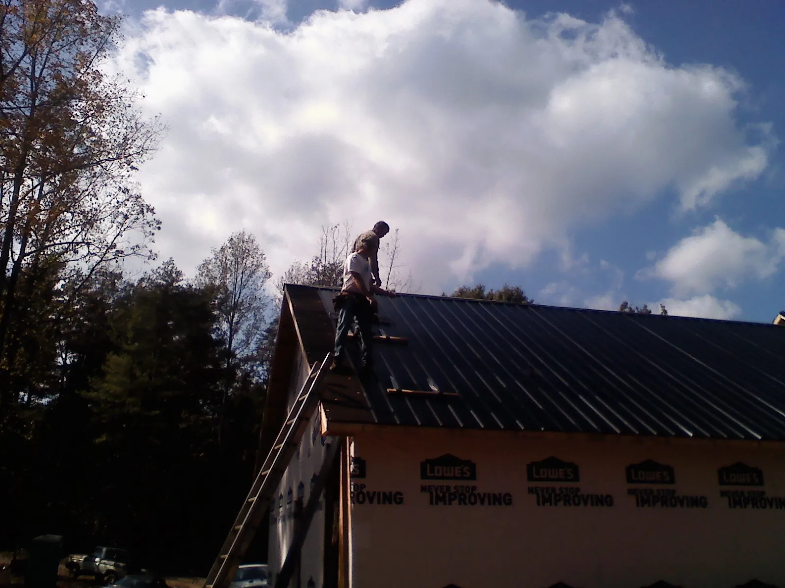 Roofer fastening dark metal panels high against a cloudy sky, from a Roof Inspection job in Tidioute