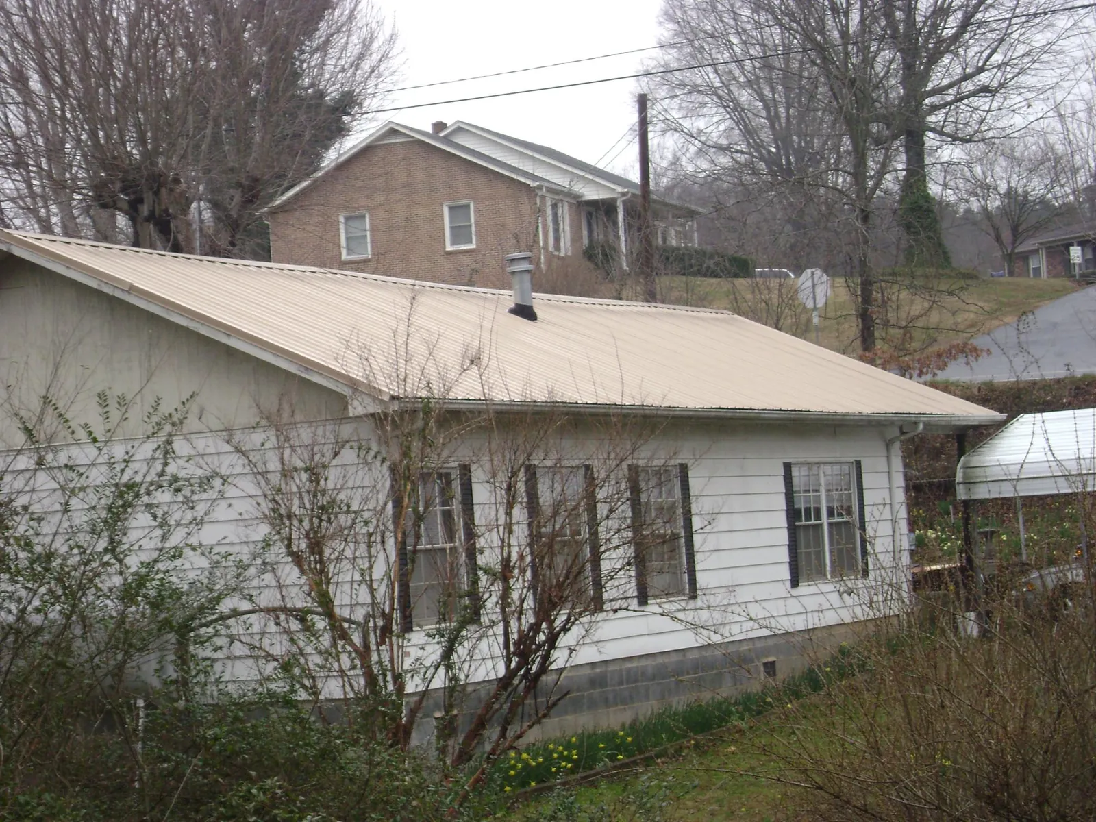 Tan metal roof on a white sided house set into a hillside — Commercial Roofing by Roofing Brothers in Tidioute